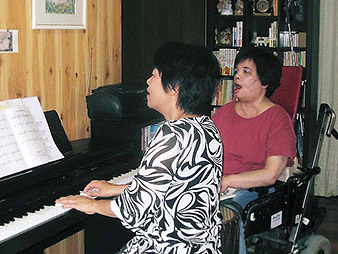 友人の弾くピアノにあわせて歌う嶋崎さんの写真