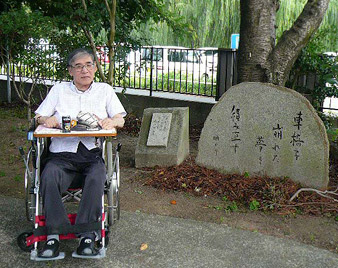 句が刻まれた石碑と車イスの浜野さんの写真