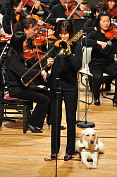 写真：トロンボーンのソロ・鈴木加奈子さん。盲導犬と一緒に