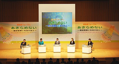写真:舞台全景。中央にスクリーン。その下に5人の出演者。