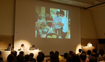 写真:会場全景。舞台背景のスクリーンに写真が投影されている。