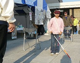 写真：目隠しをして杖を使って歩く女の子。