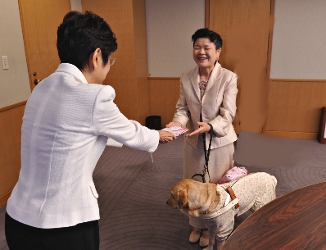 写真：盲導犬とともに目録を受け取る野田市視覚障害者協会の中村 和子さん。