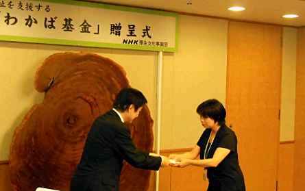写真:NHK厚生文化事業団の浅谷理事長から目録を受け取る、子どもを守る目コミュ@文京区 代表の小林 玲子さん