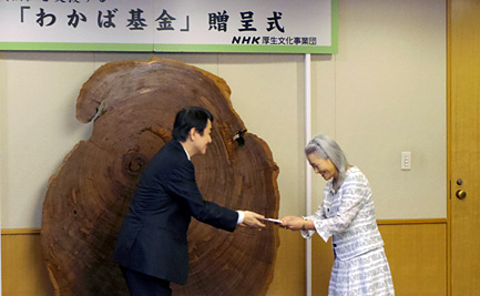 写真：NHK厚生文化事業団の浅谷理事長から目録を受け取る、あかねグループ 代表の武田 美江子さん