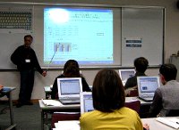 写真：パソコン講習の様子。数名の参加者がそれぞれパソコンの前に座り、講師の話を聞いている