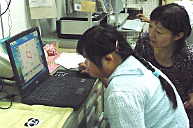 写真:パソコンで看板を製作しているやすのさんと、その様子を見守る小西 栄理さん