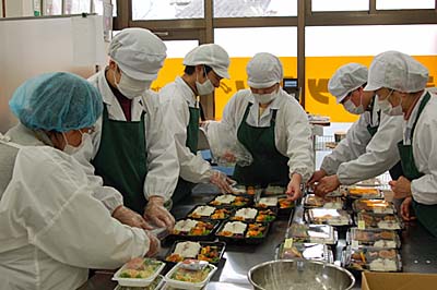 画像：弁当をおかずを盛り付けるメンバーたち
