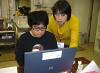 写真:パソコンを操作する障害のある人。横には他の会員が使い方を教えている。