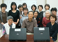 写真：パソコンを前に、記念撮影する会員たち。