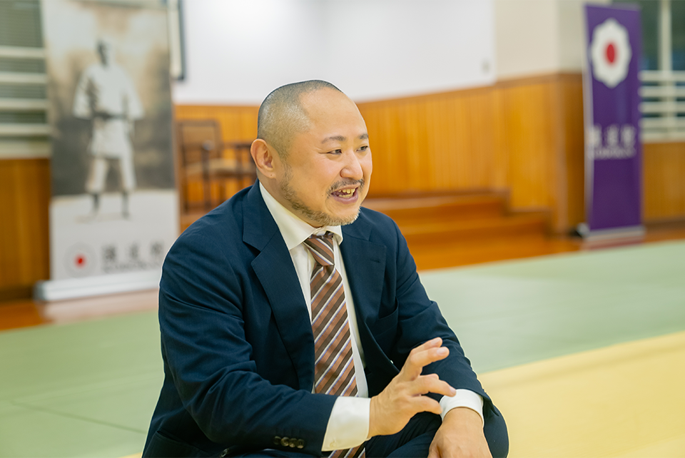 画像・講道館の畳の上、スーツ姿であぐらをかいてインタビューを受ける初瀬さん